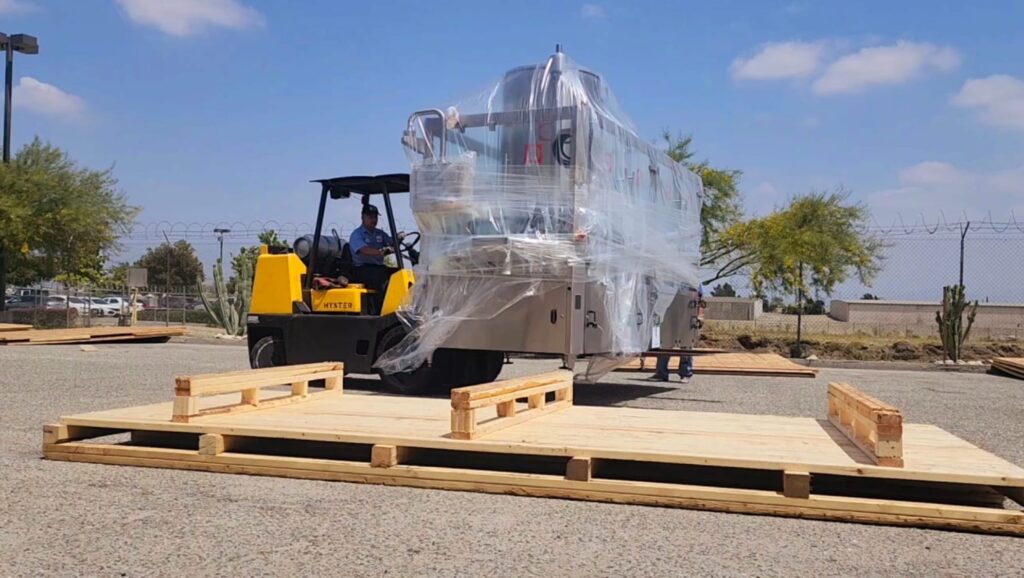 Forklift moving plastic-wrapped industrial equipment onto a wooden shipping skid